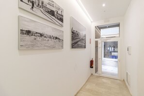 A hallway with three black and white photographs on the wall, a fire extinguisher, and a door leading outside. - Calafell Home Apartments (Calafell)