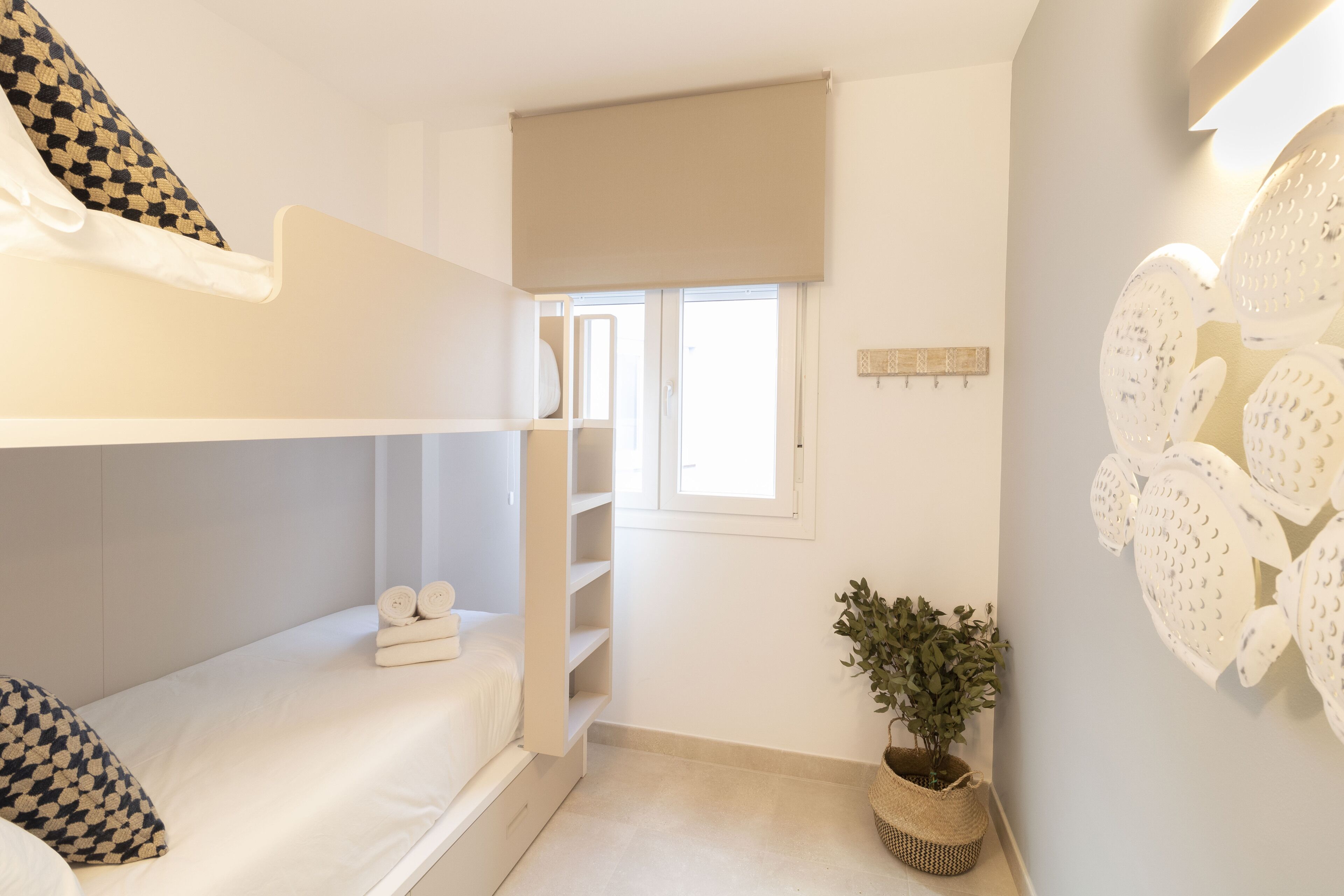 Un dormitorio con literas, una ventana pequeña, una planta y un adorno en la pared.