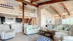 Amplia sala de estar con techo alto, una cocina al fondo y un cartel que dice "The Bell Family Beach House".