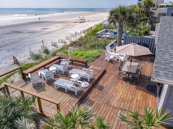 Relax on the beachfront deck with comfortable lounge chairs and tables, shaded by a large umbrella.