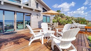 Una terraza con sillas Adirondack blancas, una mesa redonda y un paraguas grande.