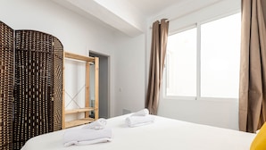 Una habitación de hotel con una cama, dos toallas enrolladas, un armario de madera y una ventana con cortinas.