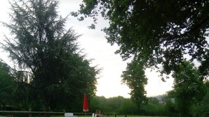 Un espace extérieur aménagé avec des chaises blanches et une table, entouré d’une clôture en bois et d’arbres.