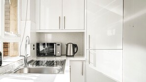 A modern kitchen with white cabinets, a stainless steel sink, a microwave, and a kettle.