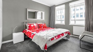 A bedroom with a bed, a nightstand, a chair, a window, and a radiator.