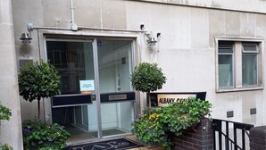 A building entrance with a glass door, a sign reading "ALBANY SCHOOLS," and a small garden area with potted plants.