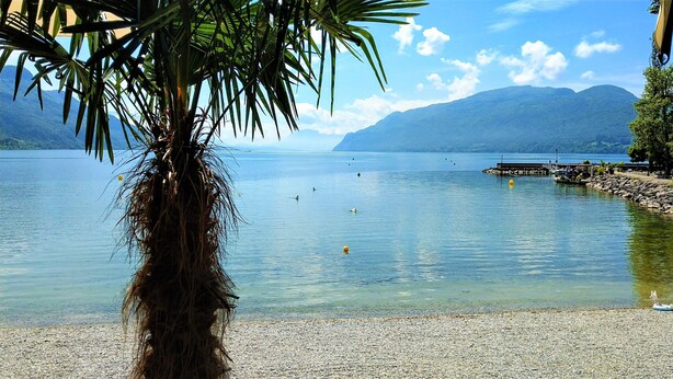 A calm lake with a pebbled shore, surrounded by mountains and a clear sky. - Cosy studio with a view, central & quiet area (Aix-les-Bains)