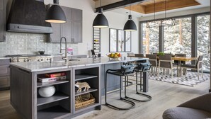 Una cocina moderna con una isla grande, luces colgantes y vistas a un comedor con un ventanal amplio.