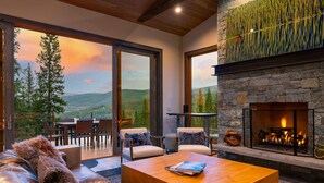 Una sala de estar moderna con chimenea, sofá de cuero, mesa de centro de madera y una vista panorámica a través de grandes ventanales.
