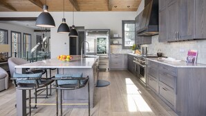 Una cocina moderna con una isla grande, iluminación colgante y armarios oscuros.