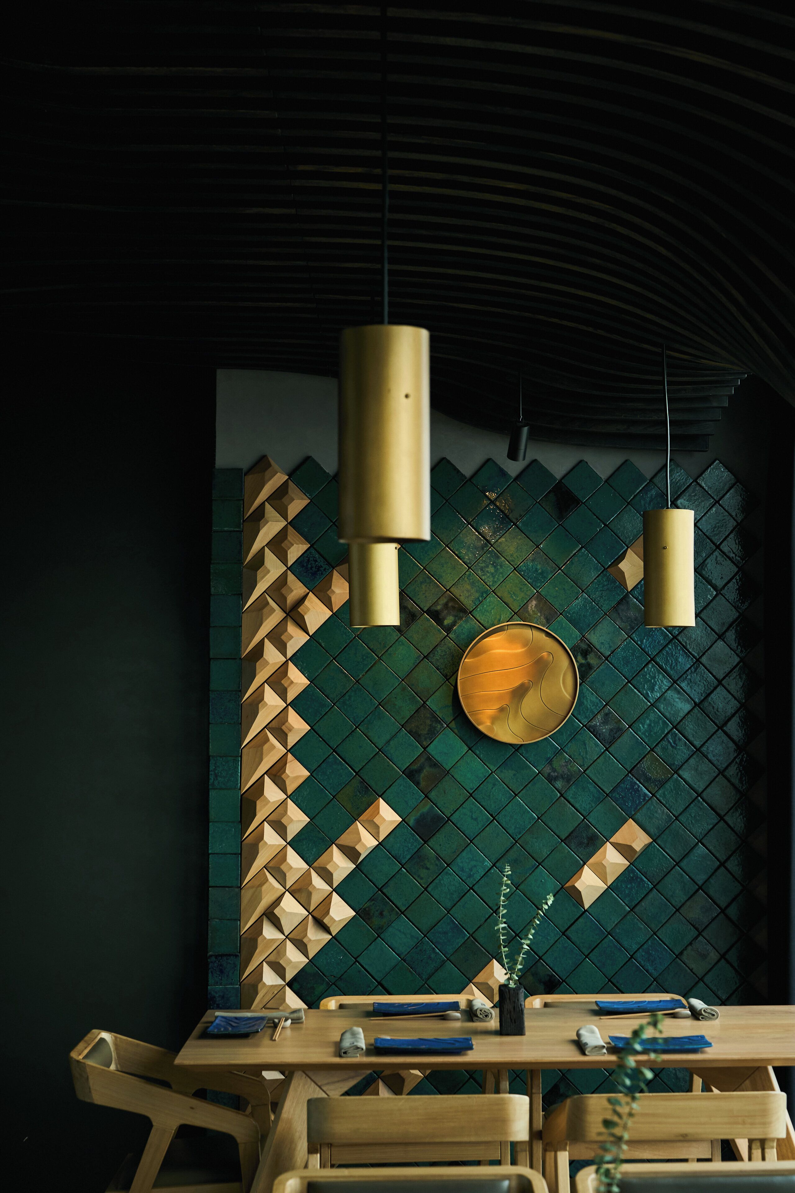 A dining area with a table set for two, a wall with a geometric pattern, and two pendant lights.