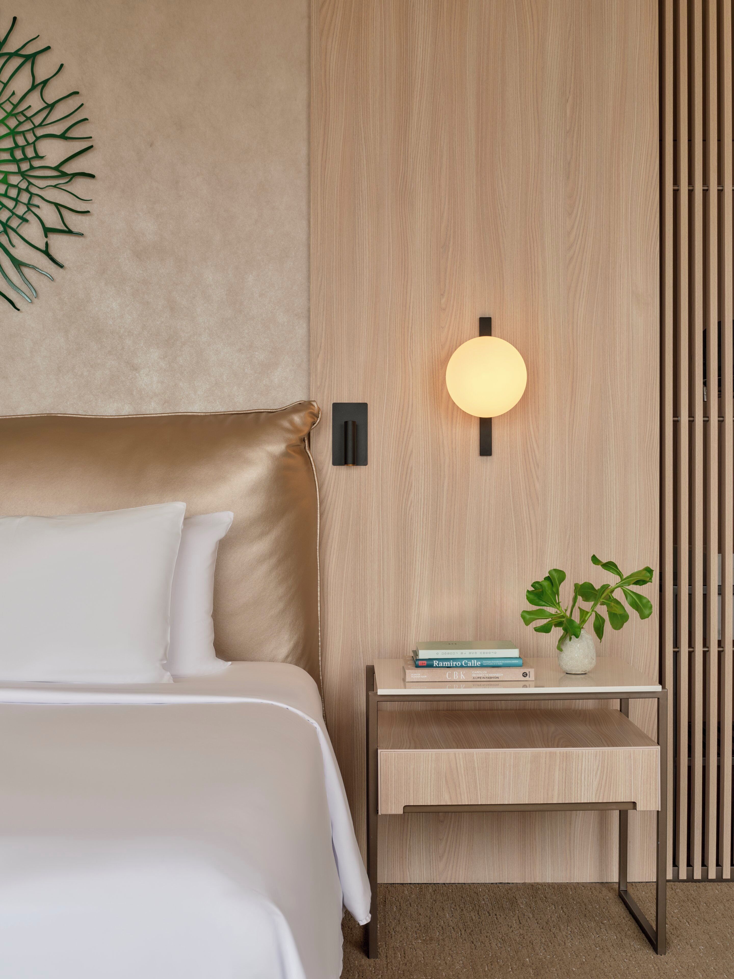 Un dormitorio moderno con cama, mesita de noche, lámpara y una planta en maceta.