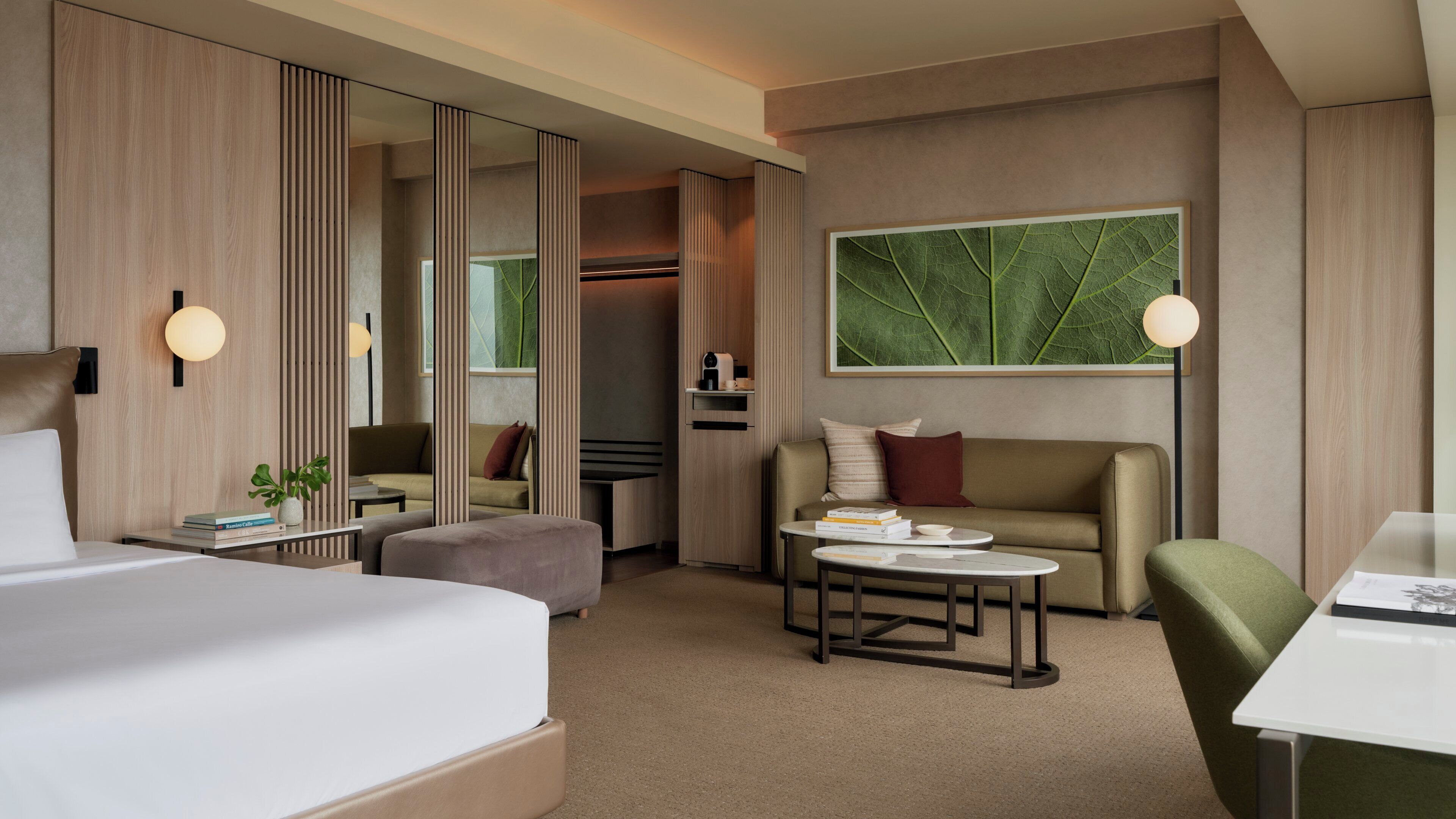 A hotel room with a bed, a sofa, a coffee table, a desk, and a large window with a leaf pattern.