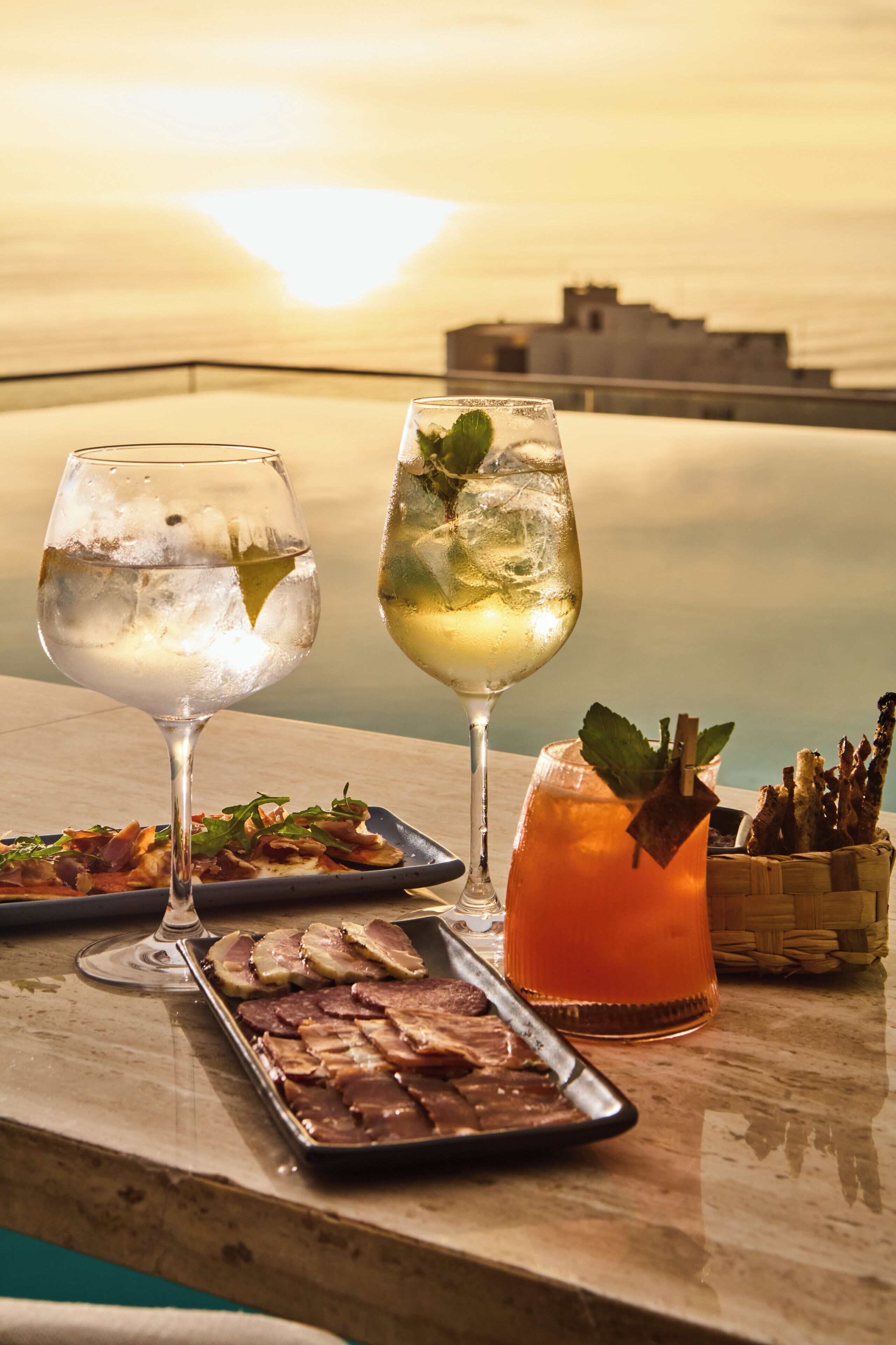 A table with two glasses of a clear beverage, a glass with a red drink, and a tray of food.