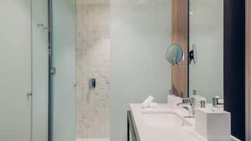 A modern bathroom with a glass shower enclosure, a marble-tiled wall, a large mirror, and a white sink with a towel.