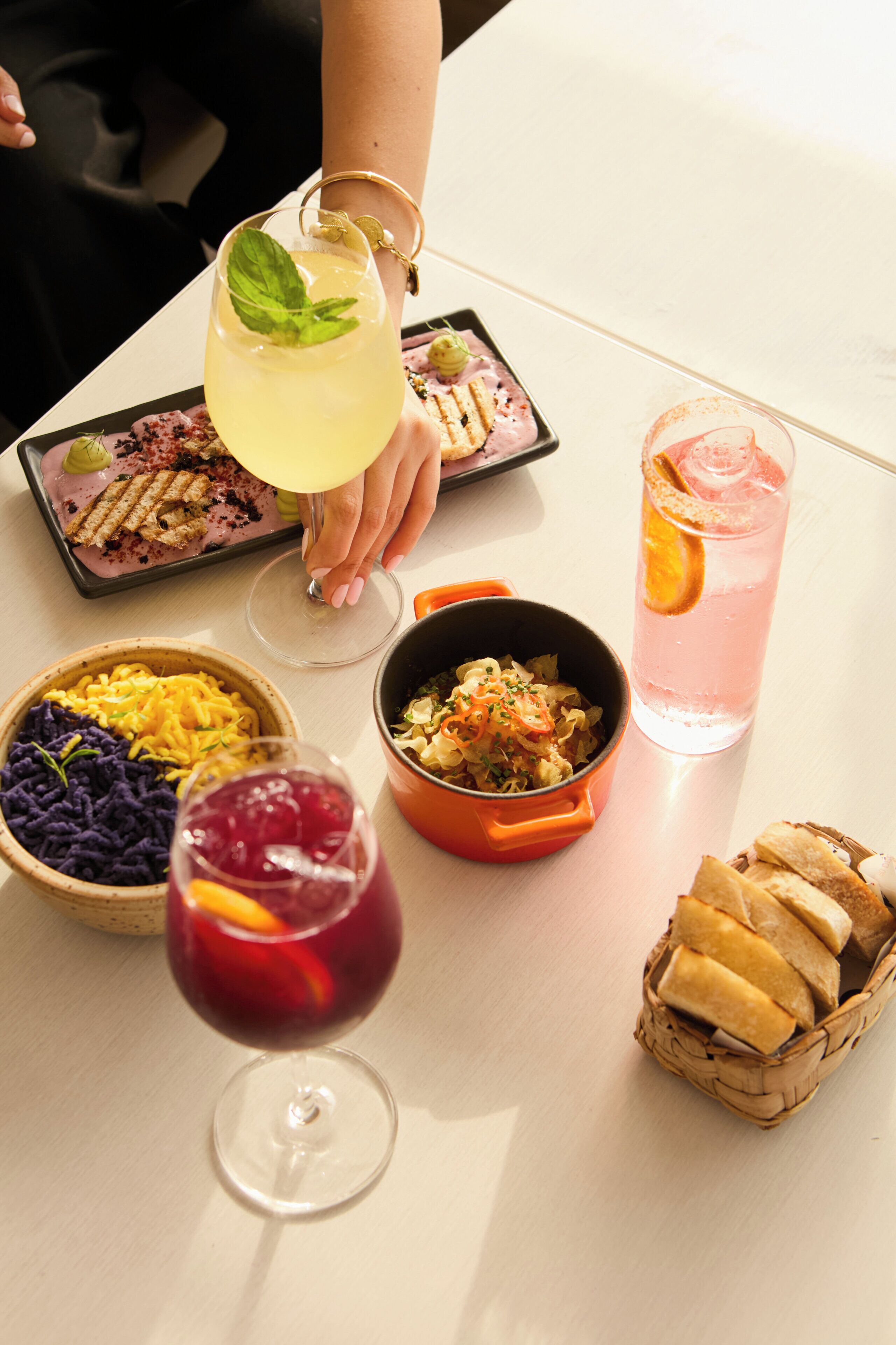 A table with various dishes, drinks, and a basket of bread.