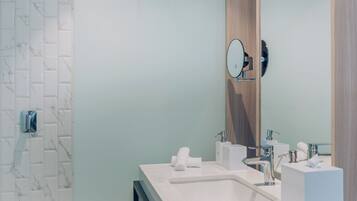 Un baño moderno con pared de azulejos de mármol, puerta de madera y lavabo blanco con espejo.