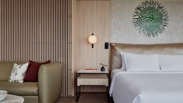 A hotel room with a bed, a sofa, a nightstand with a lamp, and a wall art piece.