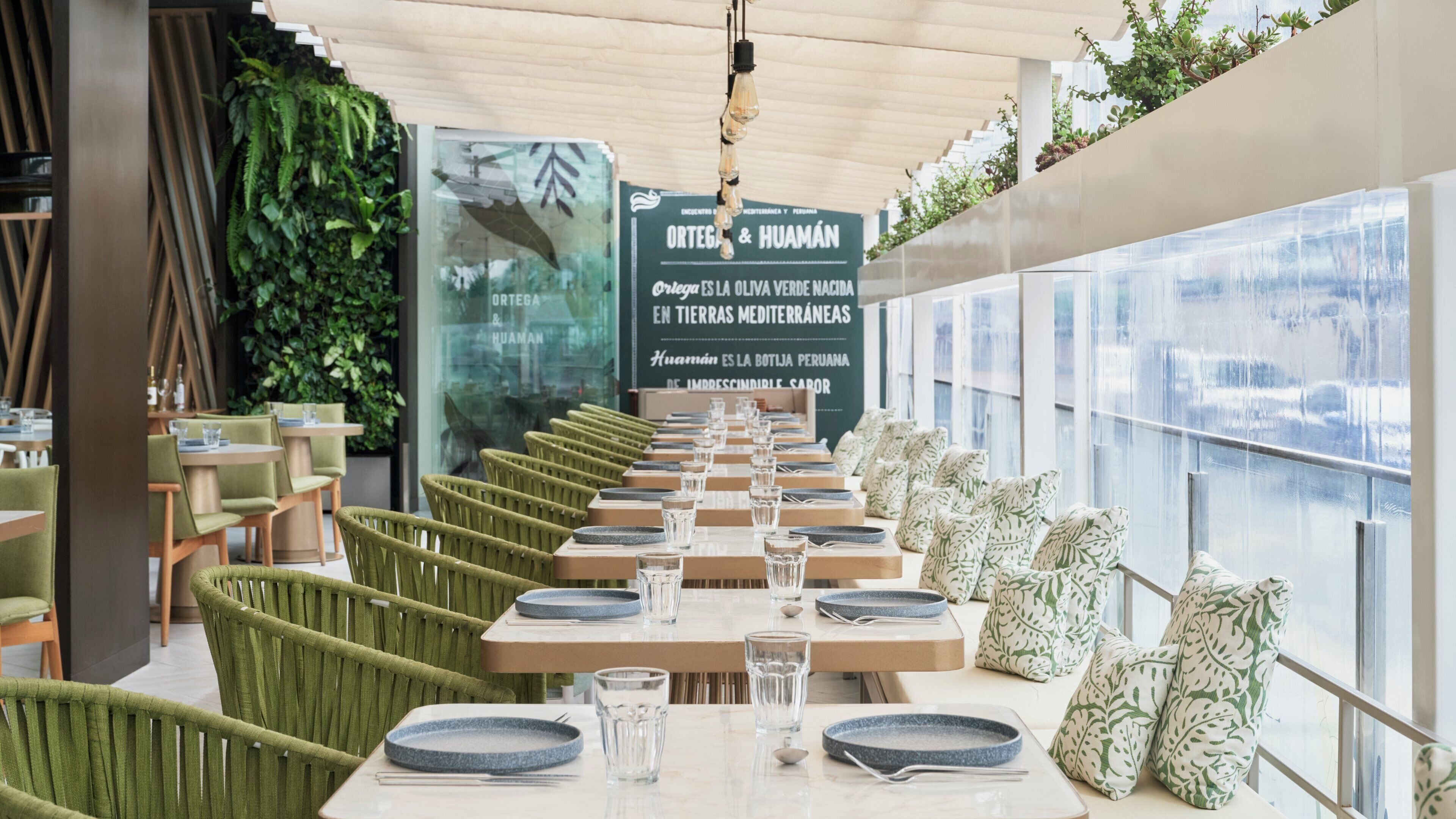 A restaurant interior with green upholstered chairs, tables with blue plates and glasses, and a large window with a view.