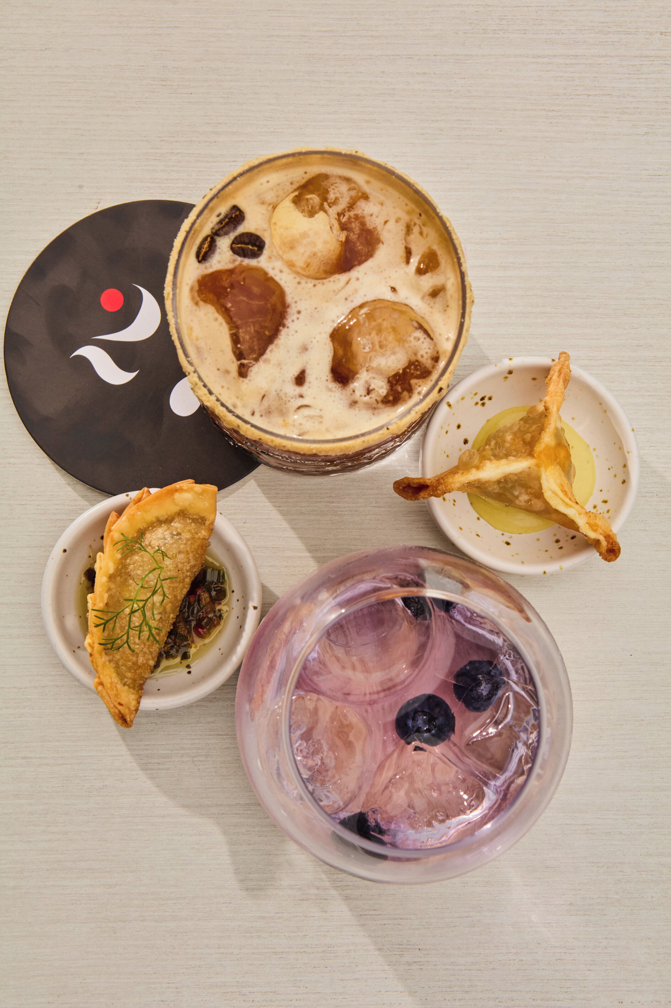 Una mesa con cuatro platos: un postre con cobertura cremosa, un bol con algo dorado, un bol con una bebida rosa y un plato con algo de color oscuro.