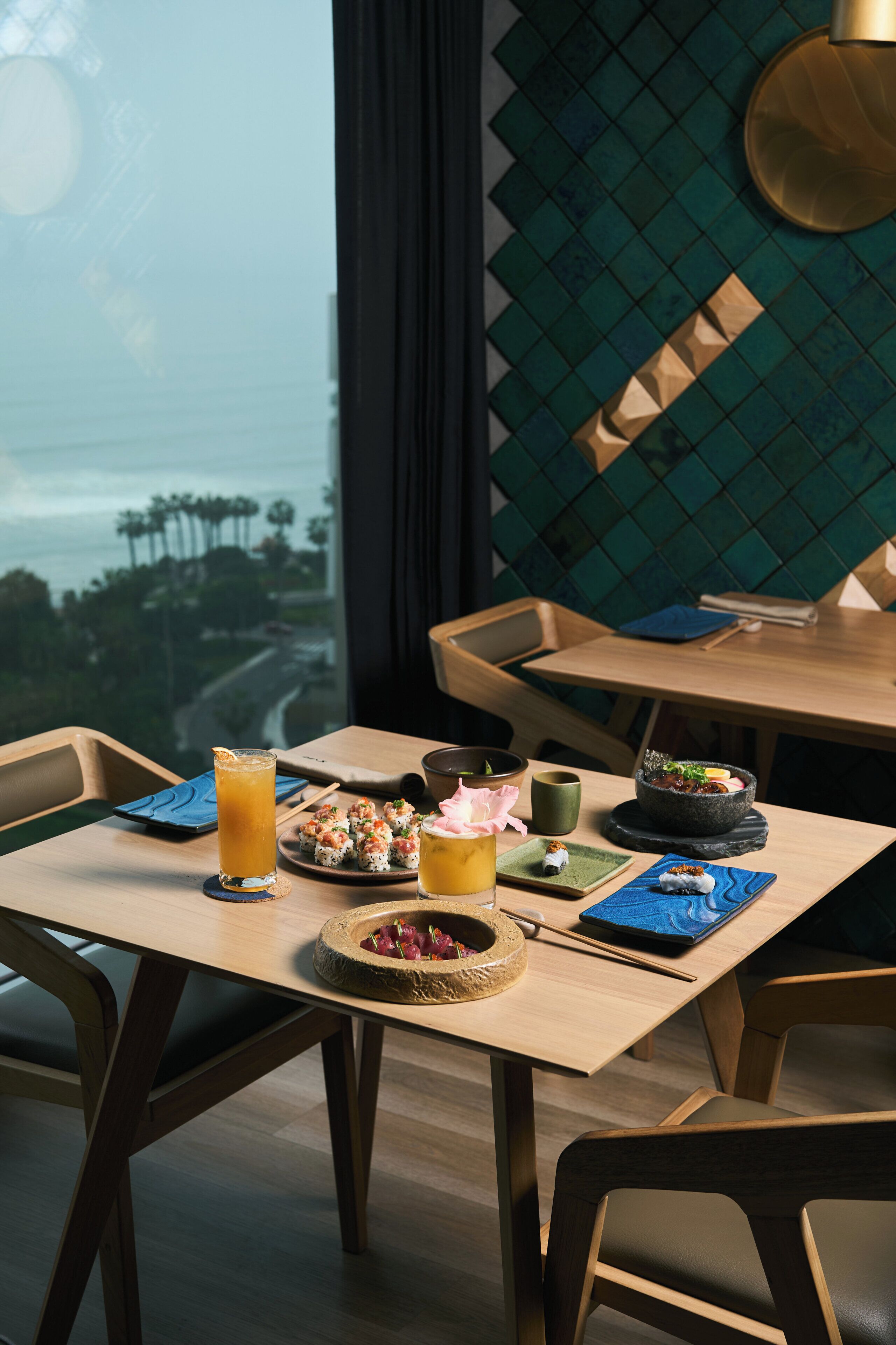 A dining table with a view of the cityscape, a bowl of sushi, a glass of orange juice, and a small dish of pickled vegetables.