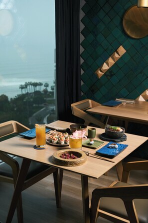 A dining table with a view of the cityscape, a bowl of sushi, a glass of orange juice, and a small dish of pickled vegetables. - Souma Hotel, Vignette Collection by IHG (Lima)