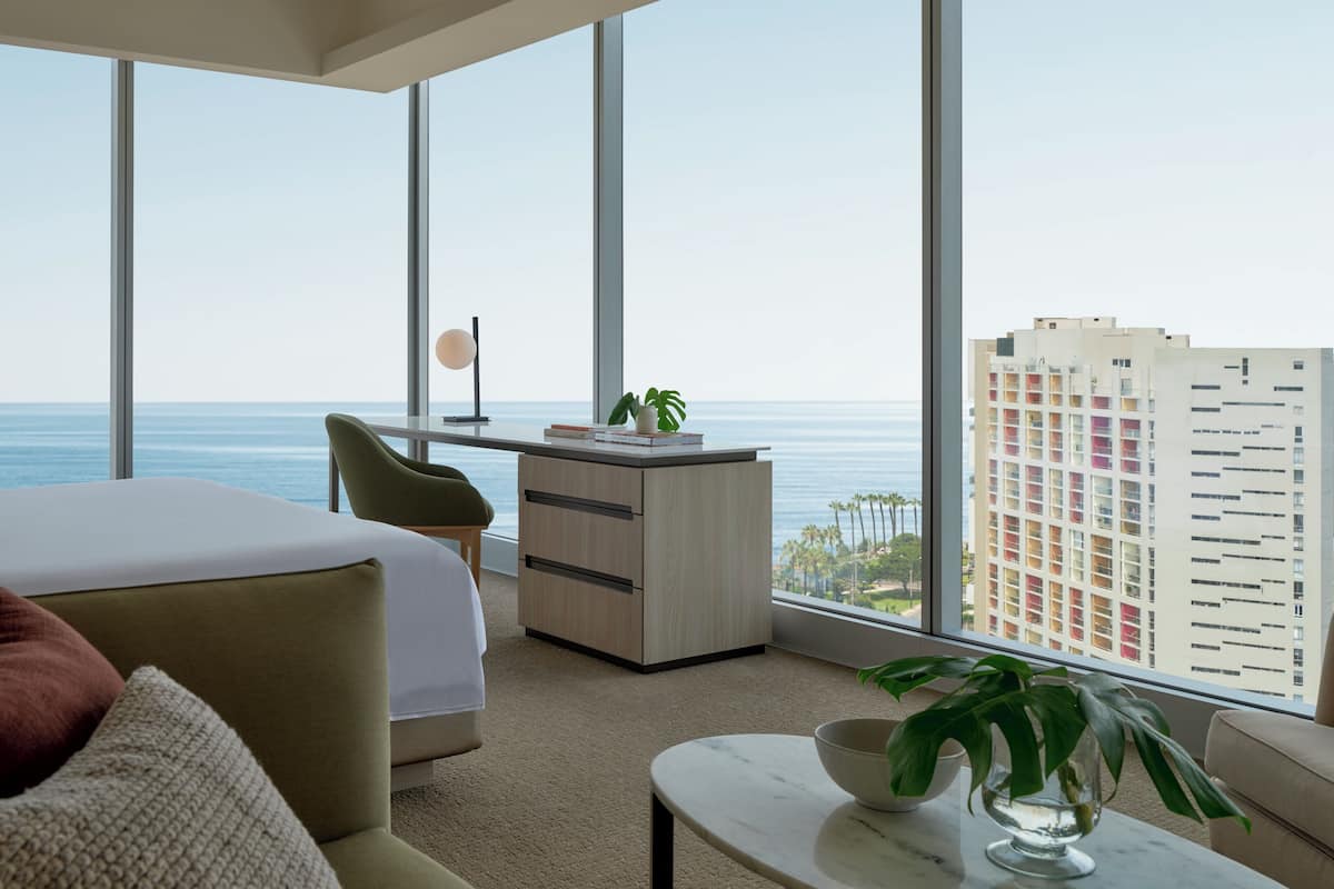 A modern hotel room with a bed, a desk, and a view of the ocean.