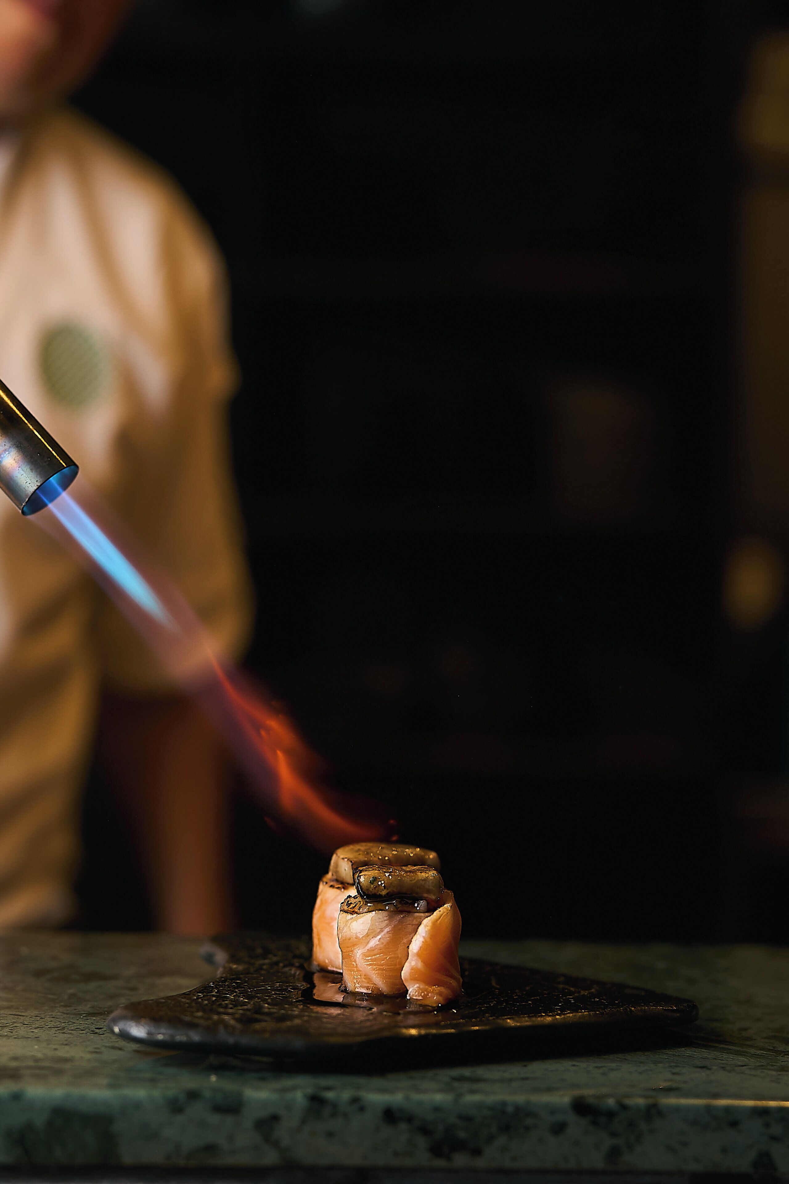 A chef cooking with a torch, focusing on a dish on a black surface.