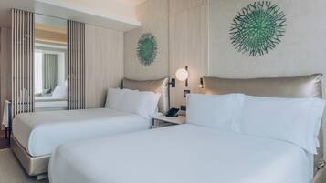 A hotel room with two beds, a mirror, a wall art piece, and a bedside table with a lamp.