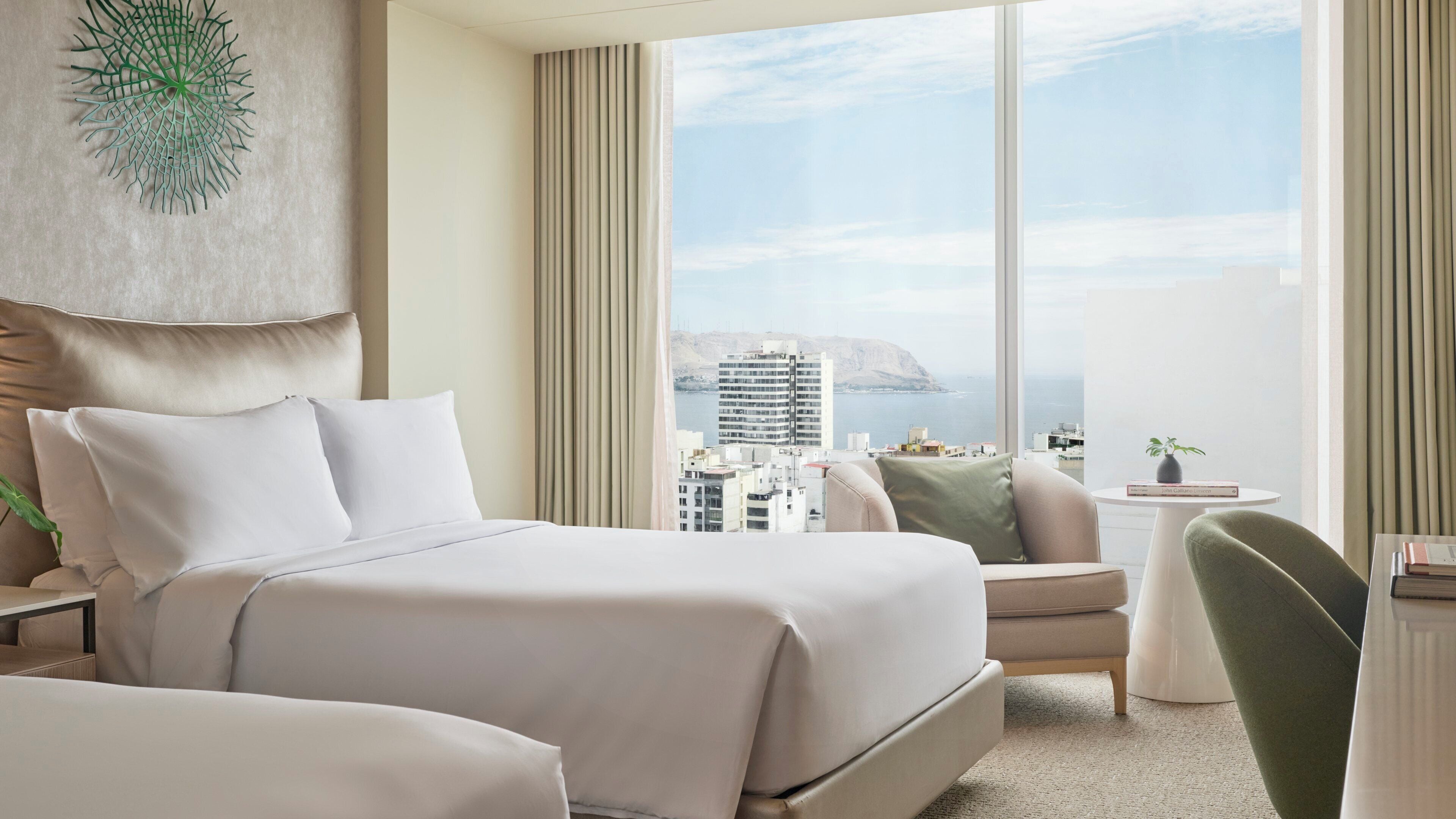 Habitación de hotel con una cama, una silla, una mesita y vistas a la ciudad.