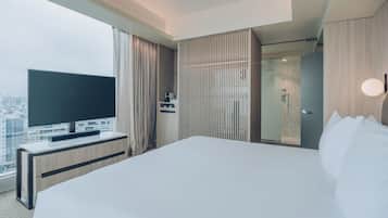 Une chambre d’hôtel moderne dotée d’un grand lit, d’un téléviseur à écran plat posé sur une console en bois, d’un dressing et offrant une vue sur la ville.