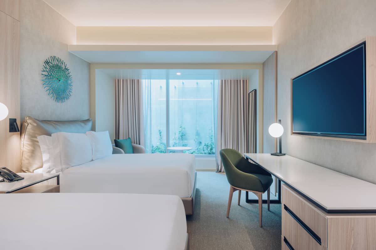 A hotel room with two beds, a desk, a chair, a TV, and a window with curtains.