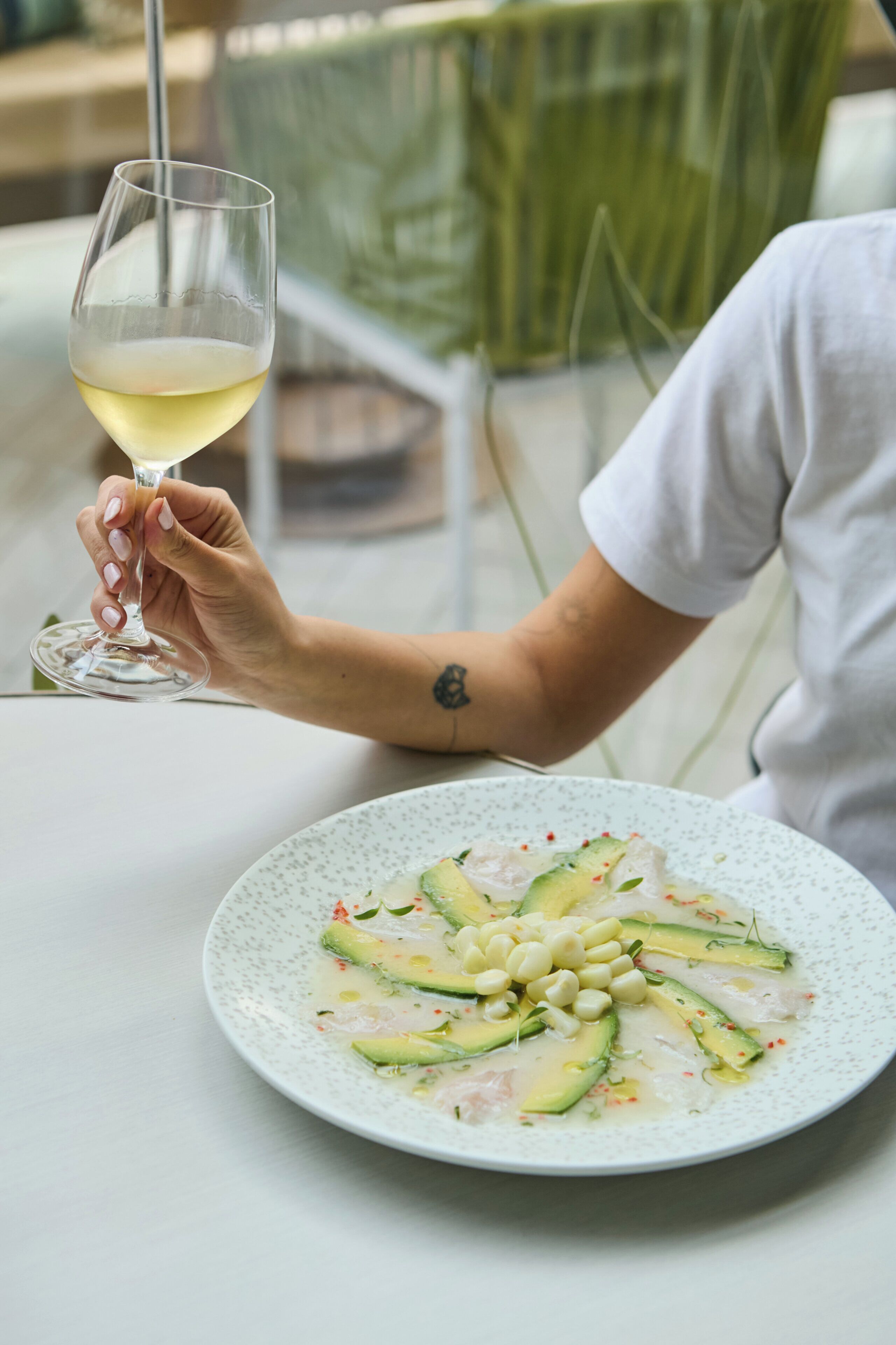 A person holding a wine glass at a table with a plate of food.