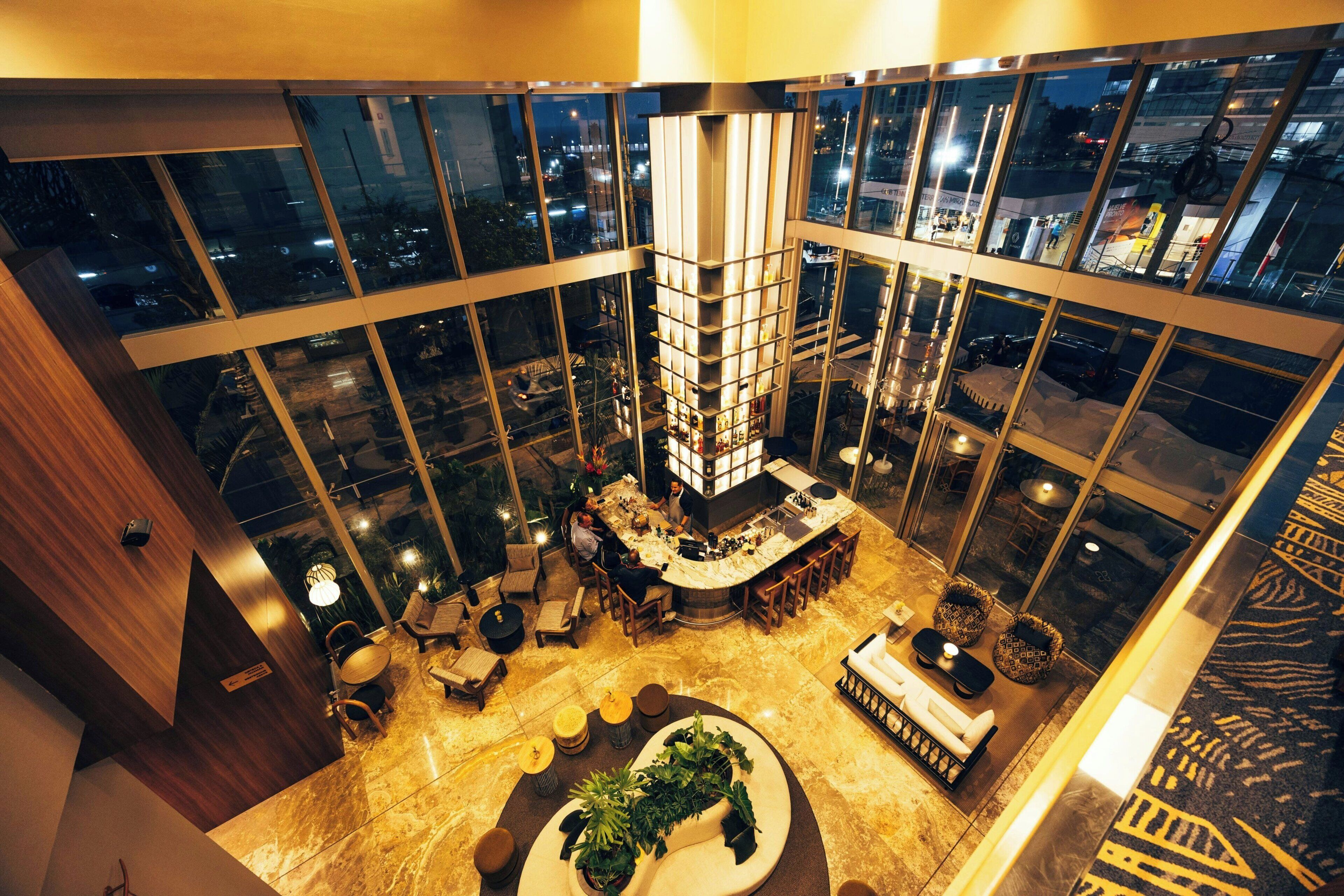 A high-rise hotel lobby with a bar area, seating arrangements, and a large window offering a city view.