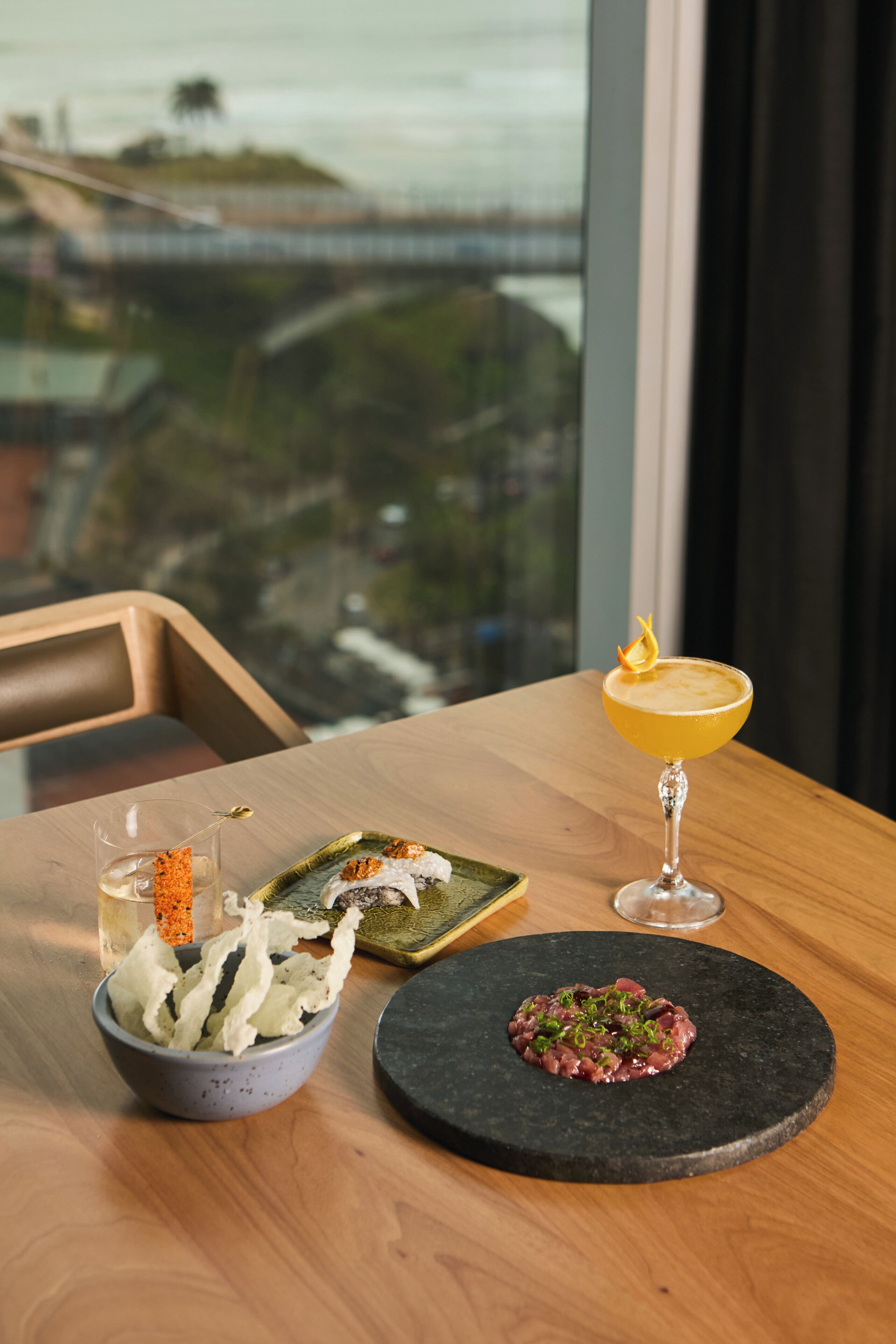 Una mesa con comida que incluye sushi, un cóctel y un cuenco de papas fritas.