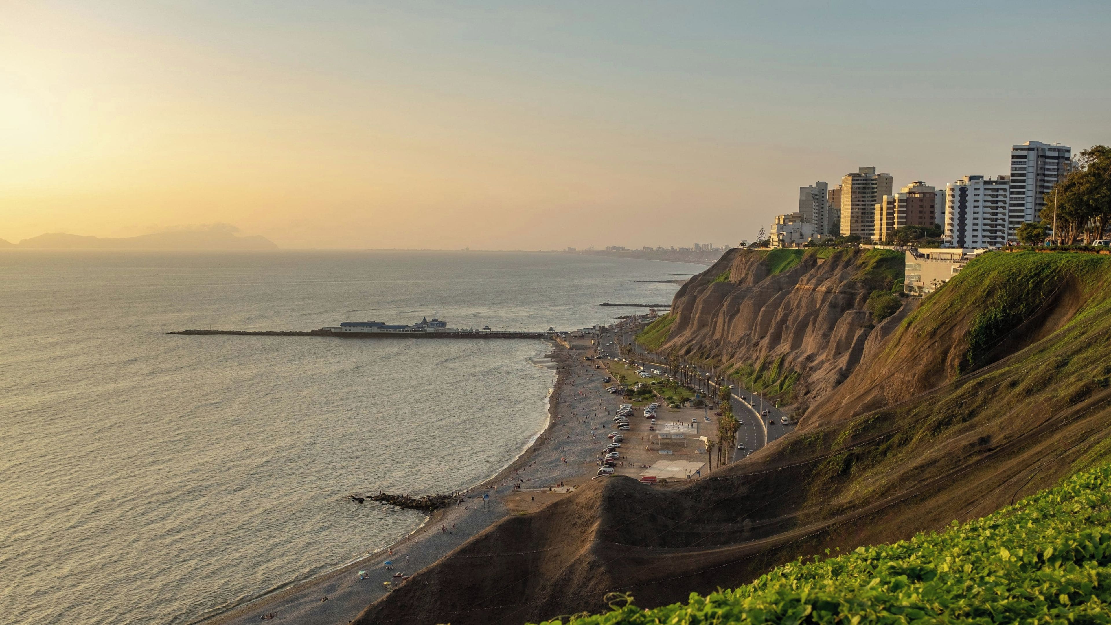 A coastal cityscape with a beach, a road along the cliff, and high-rise buildings in the background.