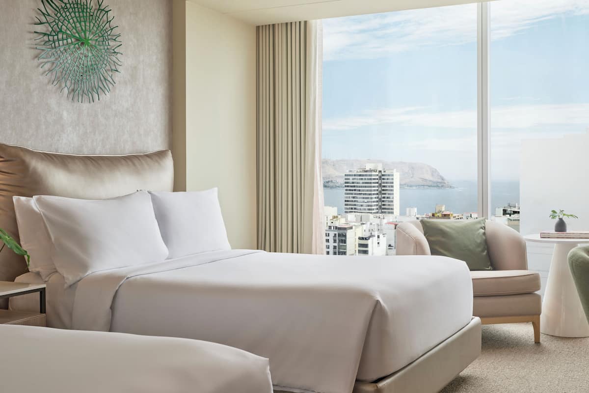 A modern hotel room with a large bed, a seating area, and a view of the cityscape.