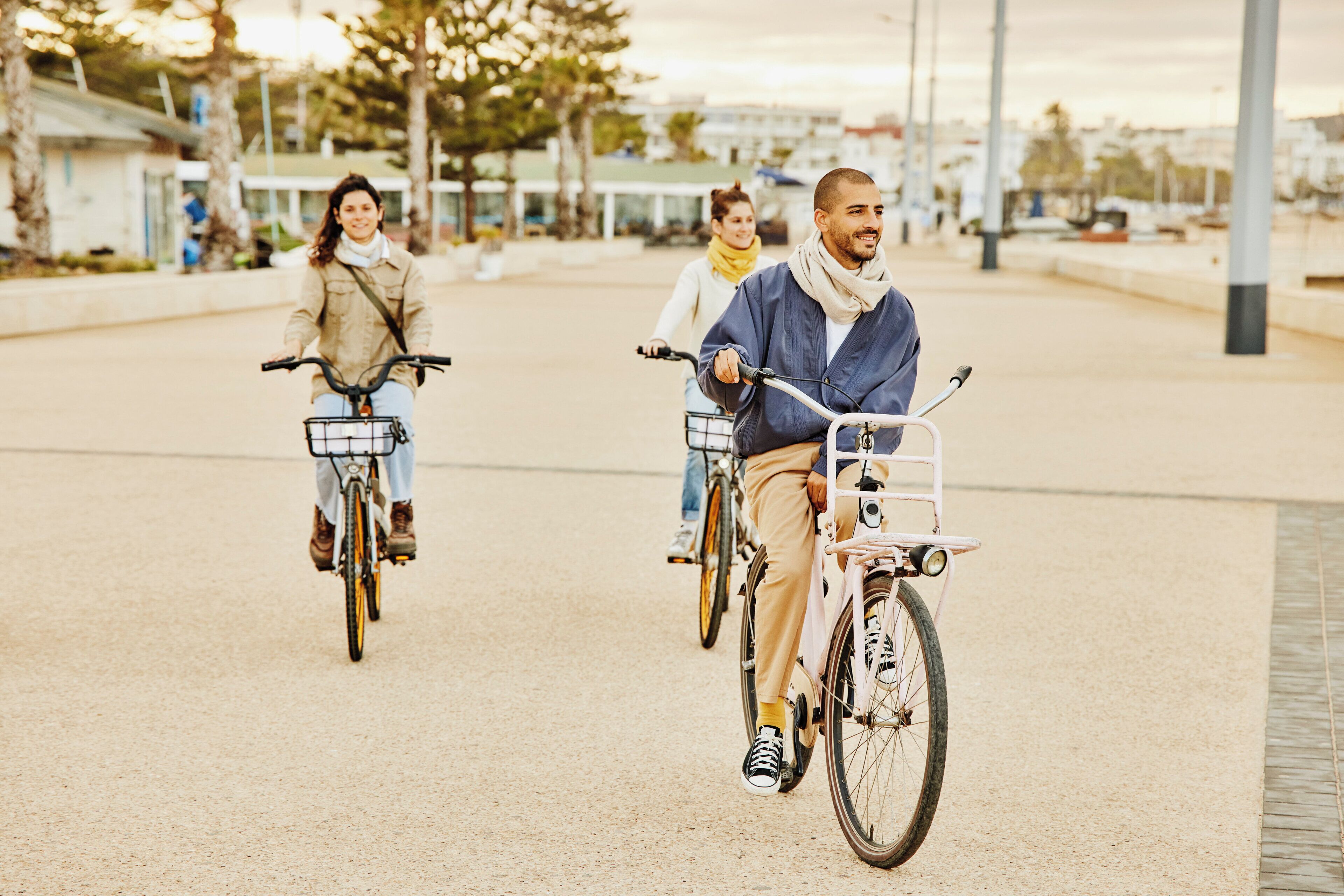 Tre personer cykler på en asfalteret sti med bygninger i baggrunden.