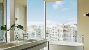 A modern bathroom with a large window, a bathtub, and two sinks.