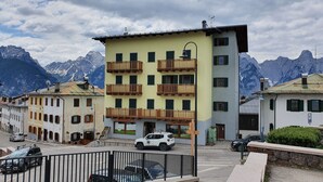 A multi-story building with balconies, a parked white SUV, and a mountain backdrop. - Casa Alpenblick, Centralissimo, Dolomiti (Danta di cadore)
