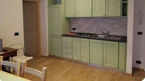 A kitchen with green cabinets, a tiled backsplash, a stove, and a hanging light fixture. - Casa Alpenblick, Centralissimo, Dolomiti (Danta di cadore)