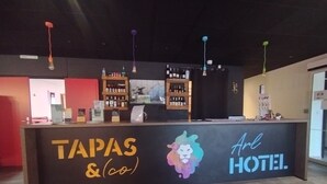 A reception desk with 'TAPAS & (co)' and 'Art Hotel' signage. There are shelves with bottles and a coffee machine. - Arl Hotel (Arles)