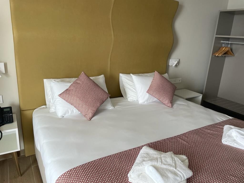 Habitación de hotel con una cama grande, dos almohadas con estampado rojo, una mesita de noche con teléfono y un armario con perchas.