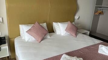 Habitación de hotel con una cama grande, dos almohadas con estampado rojo, una mesita de noche con teléfono y un armario con perchas.