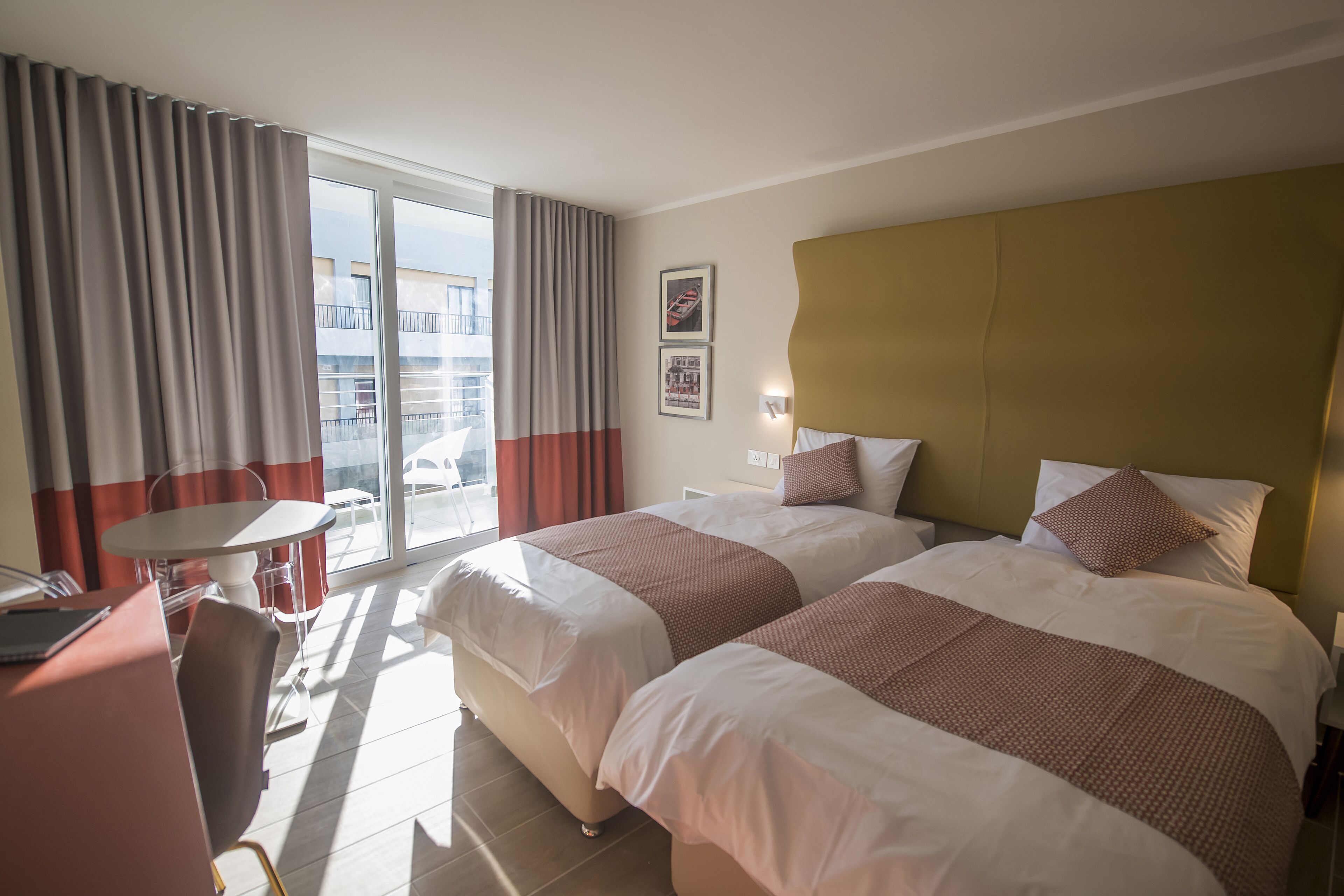 Habitación de hotel con dos camas, un escritorio, una silla y un balcón con cortinas.
