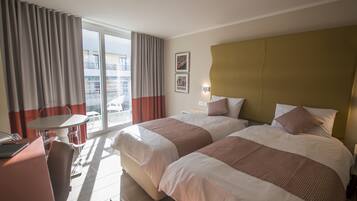 Habitación de hotel con dos camas, un escritorio, una silla y un balcón con cortinas.