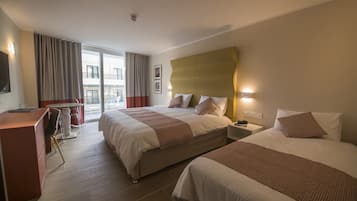 A hotel room with two beds, a desk, and a balcony with a view.