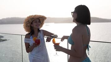 Dos personas en un balcón con vistas a un cuerpo de agua, sosteniendo bebidas.