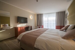 Una camera d'albergo con un letto grande, una scrivania, una sedia, una televisione e una finestra con tende.