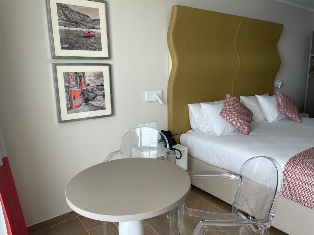 A hotel room with a bed, a round table, and two chairs. There are two framed pictures on the wall.